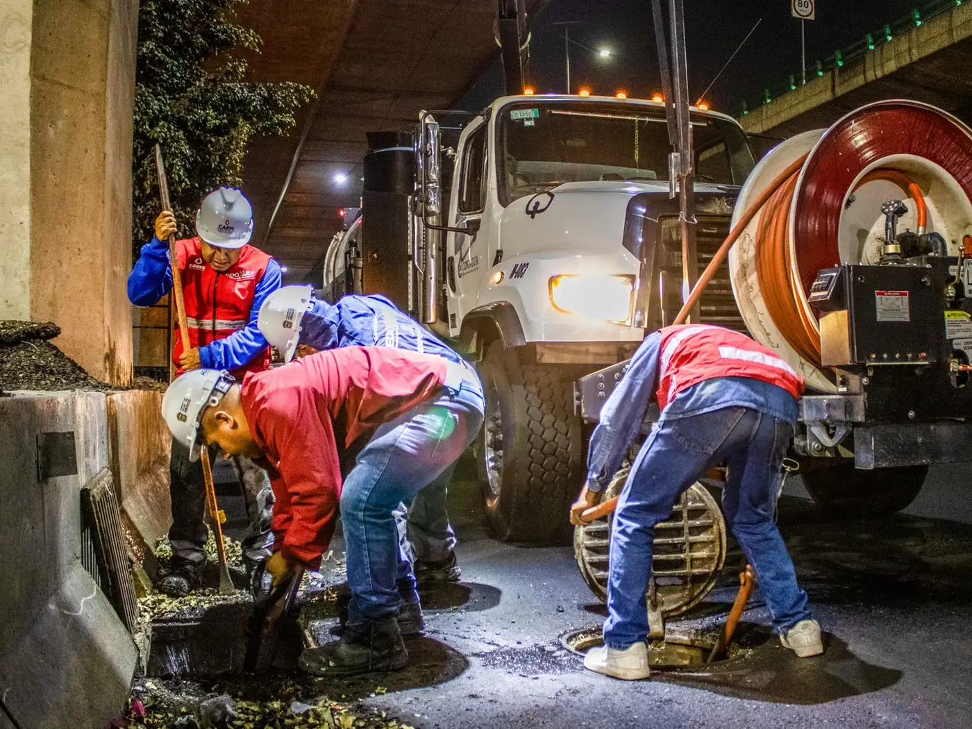 A drainage crew in hard hats clearing an open street drain beside a jetting truck