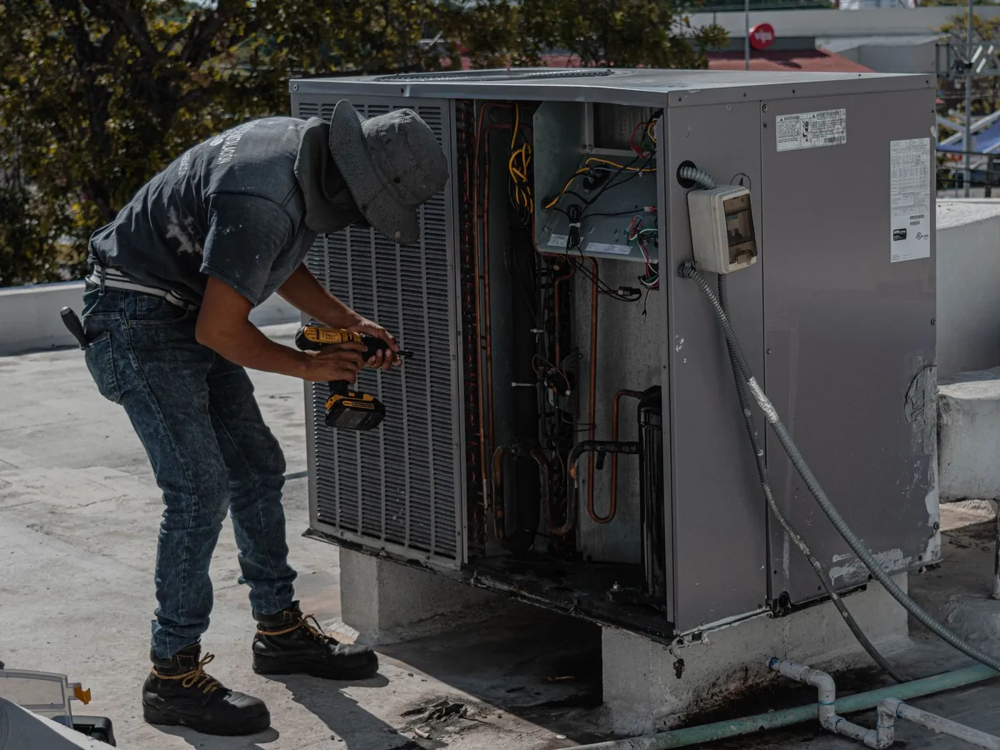 An engineer working inside an outdoor air-conditioning condenser unit on a roof