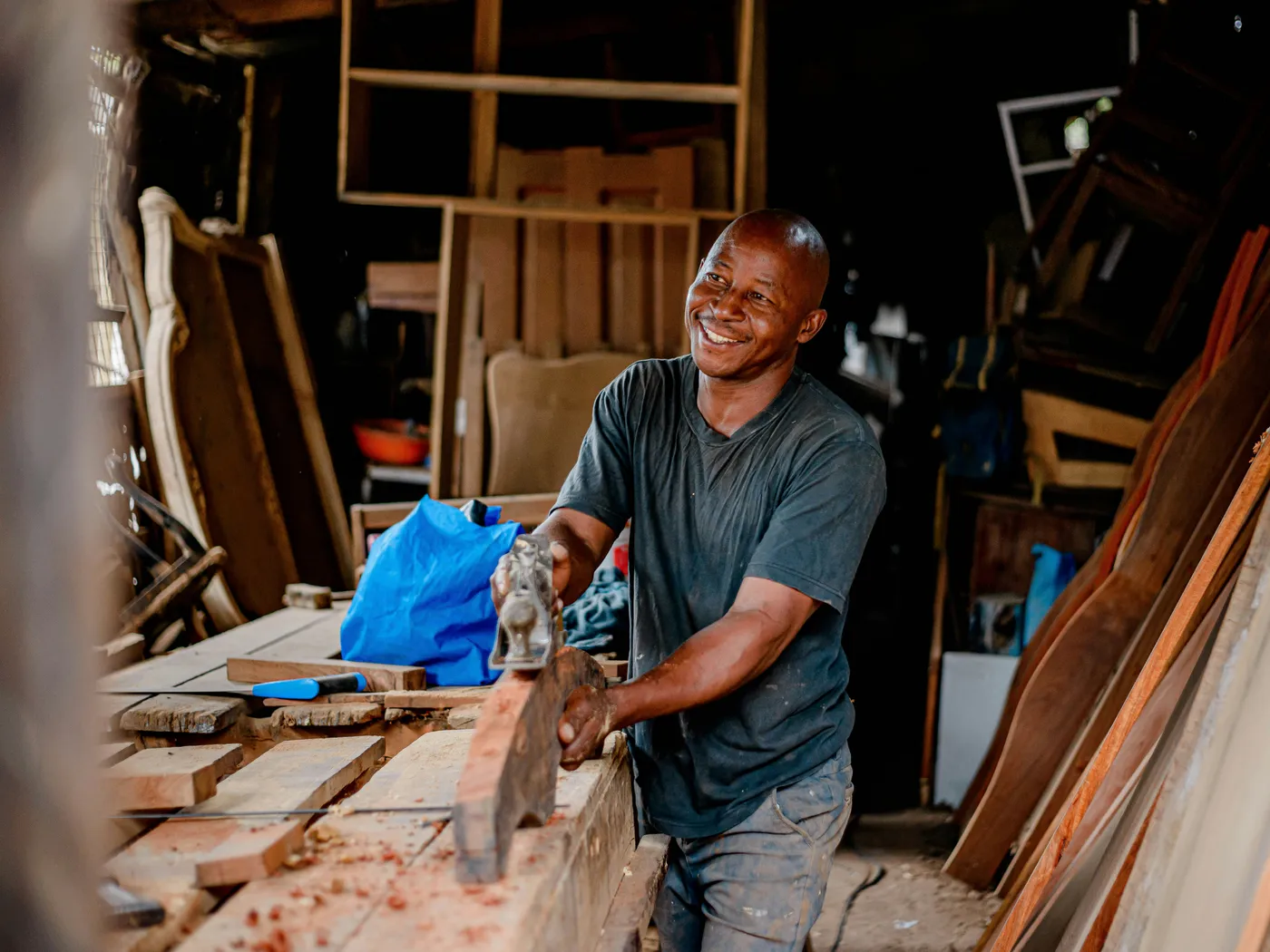 A smiling tradesman planing timber in his workshop