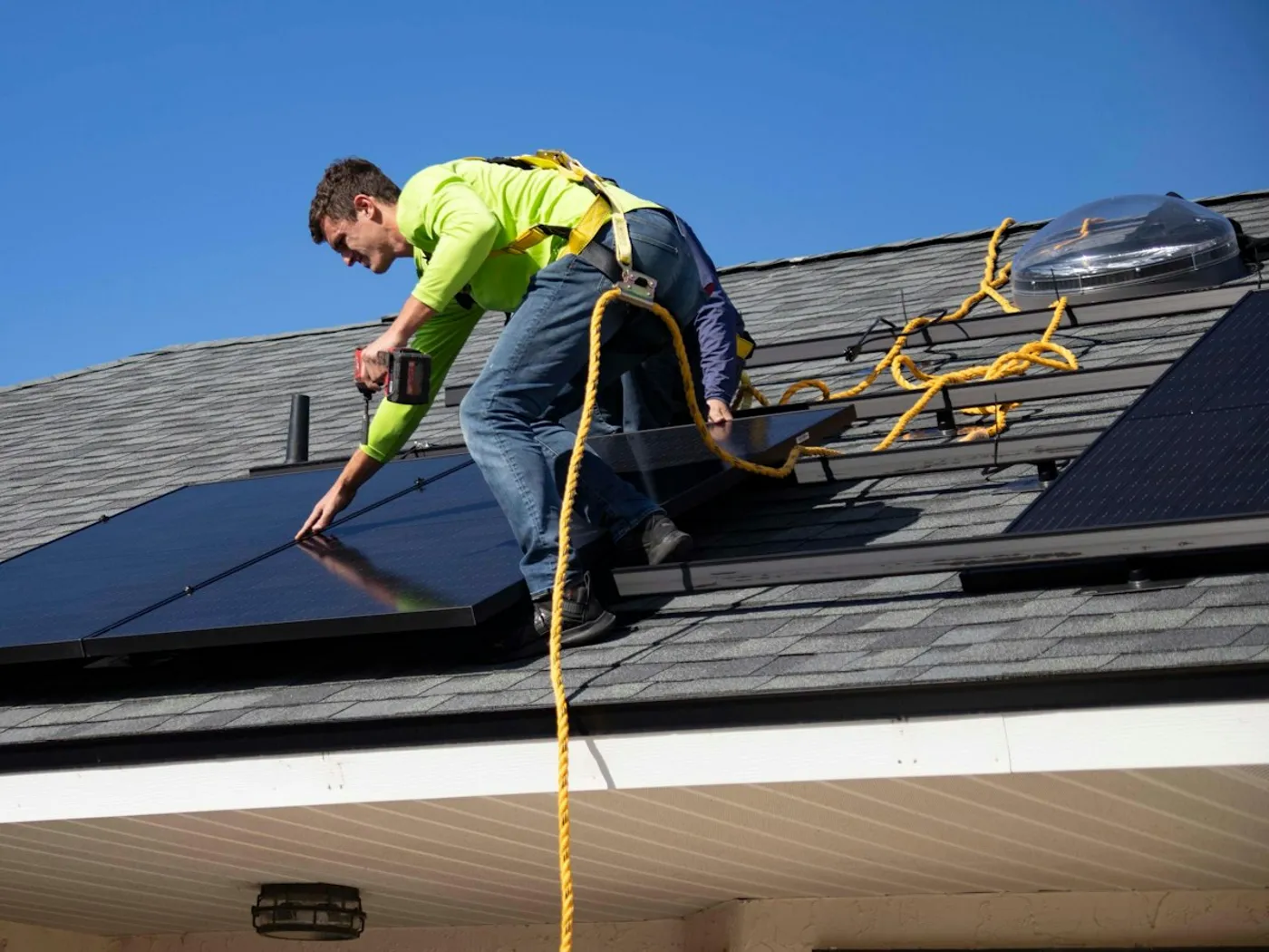 An installer in a safety harness fitting solar panels on a roof